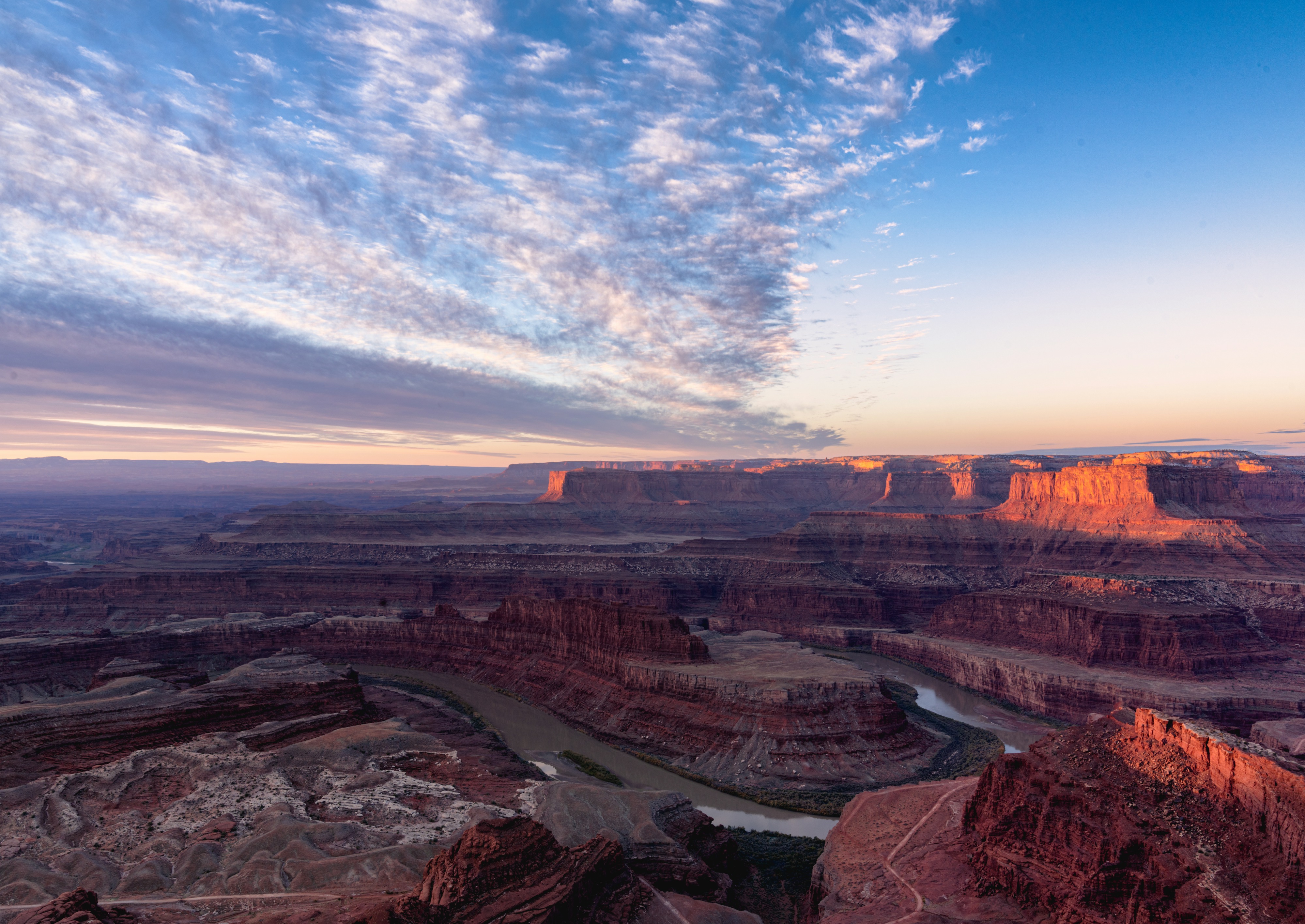 View from Dead Horse Point overlooking the Colorado River bend, layered red-rock cliffs, and a colorful evening sky