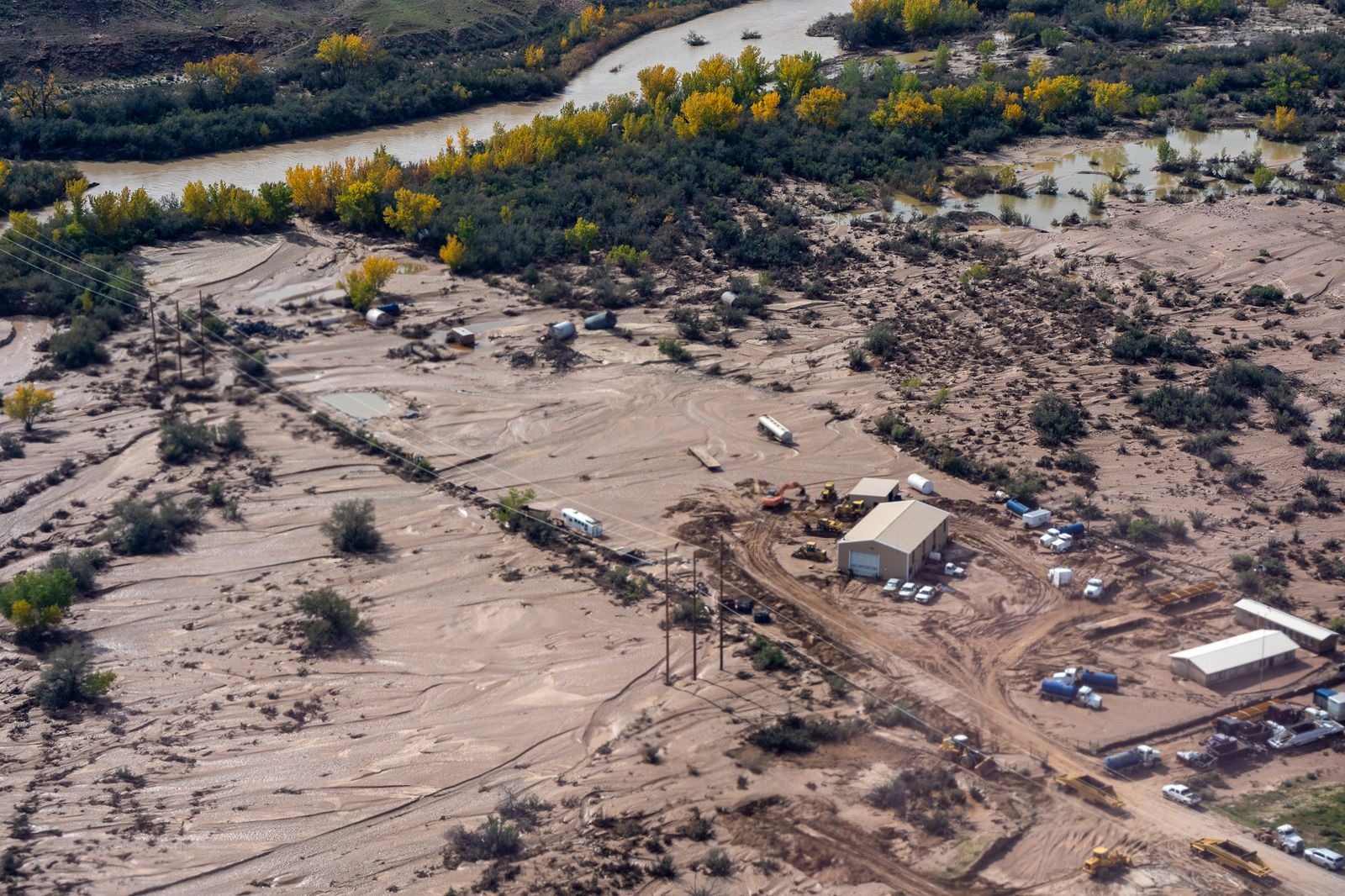 Aerial view of muddy flood deposits around buildings and equipment beside the river