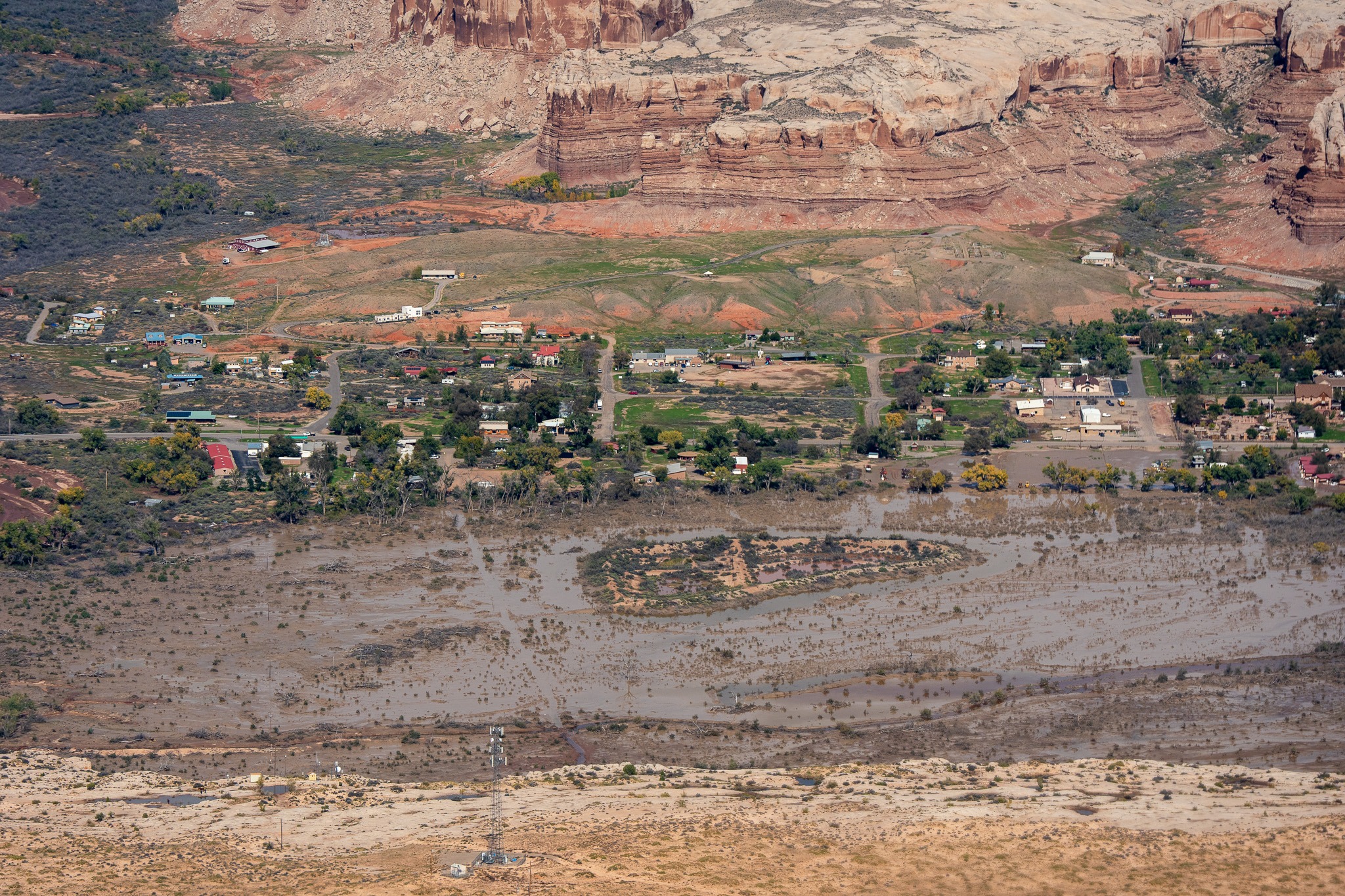 Aerial view of floodwater near homes beneath red-rock cliffs
